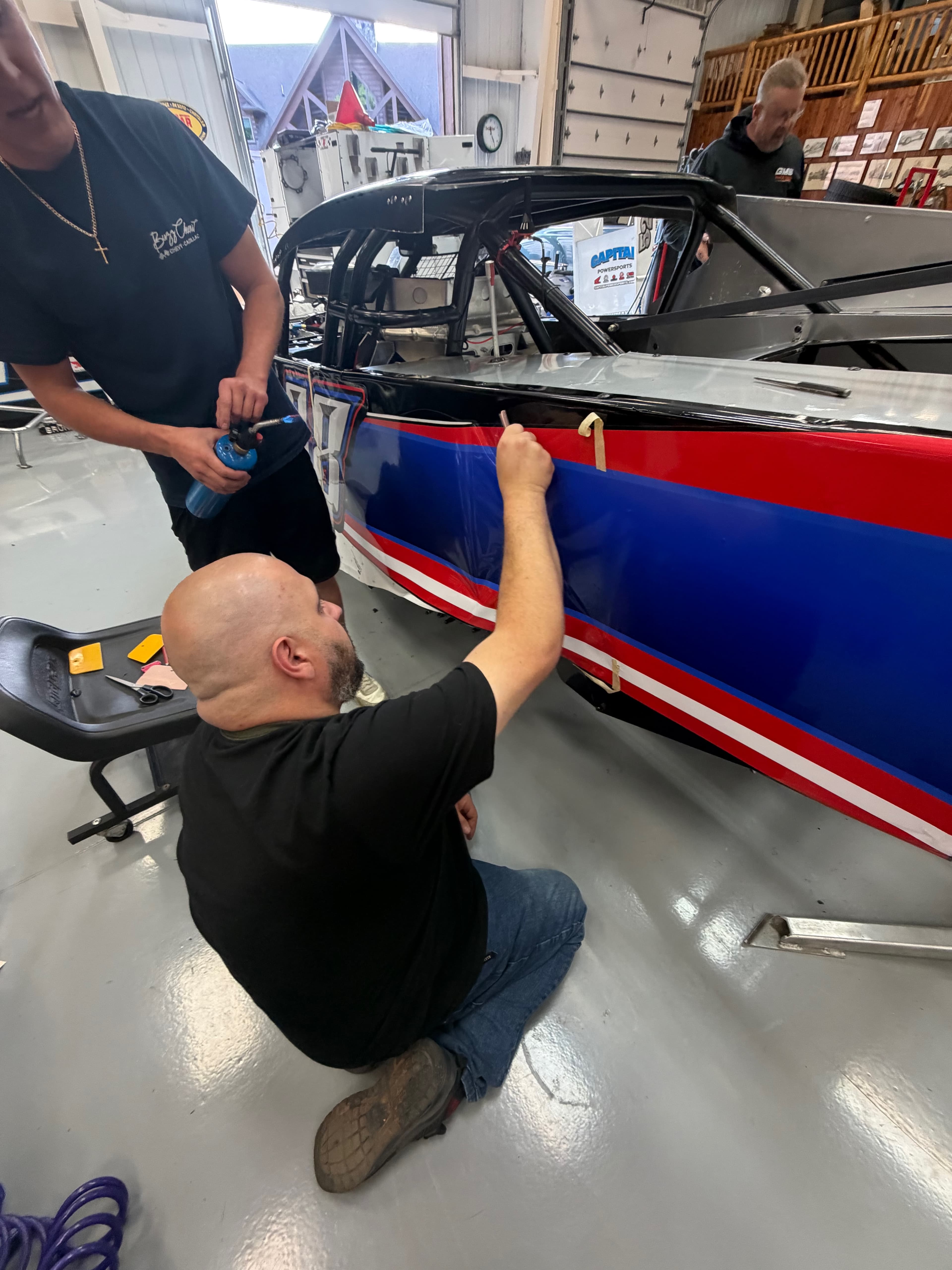 Applying vinyl wrap to race car in the shop